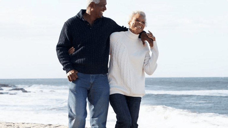 Elderly couple strolling along beach laughing together Elderly couple strolling along beach laughing together